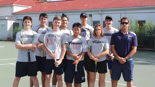 El grupo de tenis de la Florida Preparatory Academy posa junto en la cancha de tenis frente a un edificio escolar.
