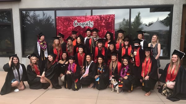 Un gran grupo de mayormente mujeres jóvenes está de pie frente a un fondo rojo de Foothill College con la inscripción 'Congrats'.