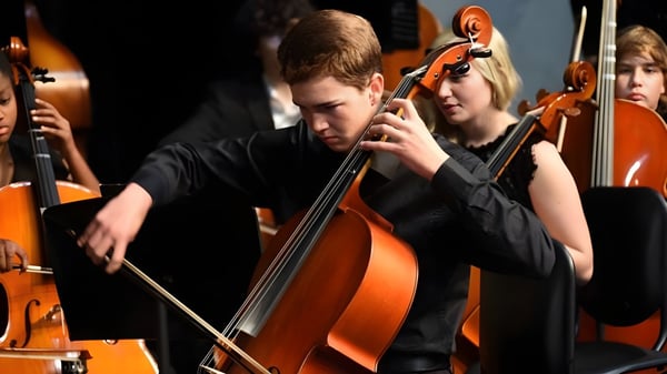 Un estudiante de la Forsyth Country Day School toca el violonchelo concentrado en un escenario con otros músicos de instrumentos de cuerda.