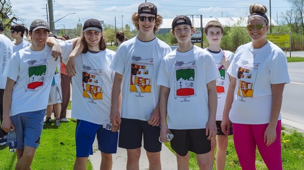 Un grupo de estudiantes de la Fort Erie International Academy está juntos al aire libre en un campo con árboles de fondo.