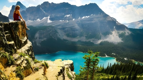 Una persona mira desde un acantilado rocoso hacia un lago turquesa y montañas cubiertas de nieve en los alrededores de la Fort Erie International Academy.