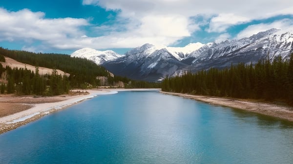 Un tranquilo río turquesa fluye a través de un paisaje montañoso con picos nevados bajo un cielo nublado.