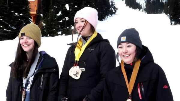 Tres estudiantes de la Fort St. James Secondary están vestidos para el invierno afuera en un paisaje nevado con árboles.