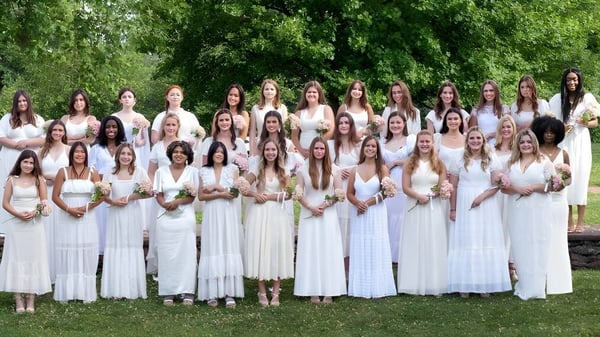 Un grupo de alumnas de la Foxcroft School lleva túnicas romanas blancas y está juntas en el área exterior verde.