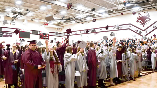 Un gran grupo de estudiantes de la Fox Valley Lutheran High School está en sus togas de graduación en un salón decorado.