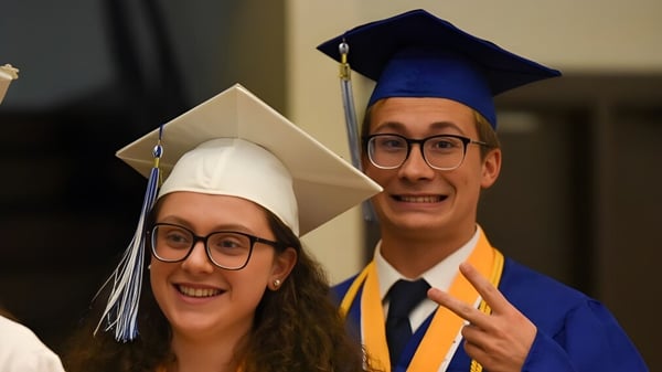 Dos graduados de la F.P. Walshe School en ropa de graduación están juntos en un interior.