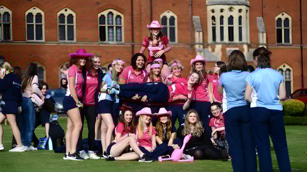 Un grupo de estudiantes femeninas en atuendos rosas está en una pradera frente a un edificio de ladrillo en el campus del Framlingham College.