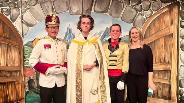 Cuatro estudiantes del Francis Douglas Memorial College están en coloridos disfraces frente a un fondo rústico de madera.