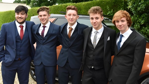 Estudiantes del Franciscan College Gormanston están en ropa formal frente a un auto rodeados de vegetación verde.