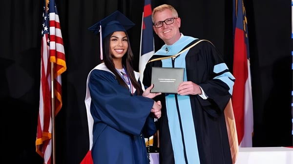Una graduada de la Freedom Christian Academy le da la mano a un hombre con toga académica después de la ceremonia de graduación.