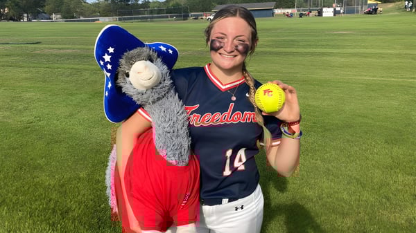 Una estudiante sonriente de la Freedom Christian Academy está en el campo de softbol sosteniendo una pelota de softbol en la mano.