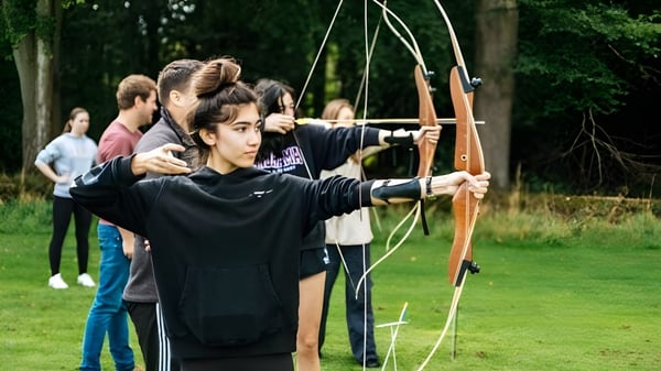 Estudiantes de la Frensham Heights School practican tiro con arco en un campo cubierto de hierba con árboles al fondo.