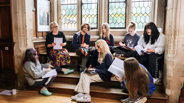 Un grupo de estudiantes se sienta en las escaleras frente a un antiguo edificio con ventanas de colores en el campus de la Frensham Heights School.