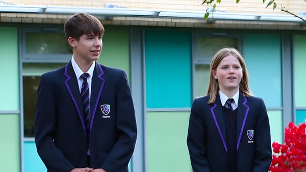 Dos estudiantes en uniformes escolares están de pie frente a un edificio verde en el campus del Frome College.