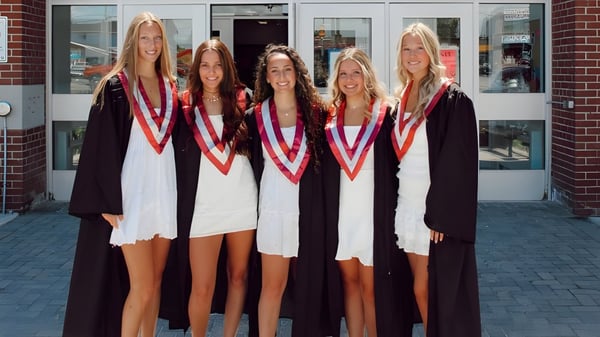 Cinco egresadas están frente a un edificio de ladrillo en el campus de la Frontenac Secondary School celebrando su graduación.