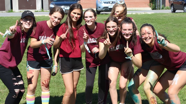 Un grupo de estudiantes en camisetas rojas posan sobre el césped frente a un edificio de ladrillo de la Frontenac Secondary School.