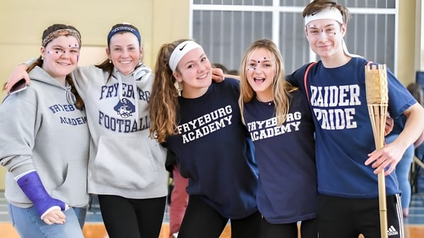 Un grupo de cinco estudiantes se agrupan y sonríen en el campus de la Fryeburg Academy.