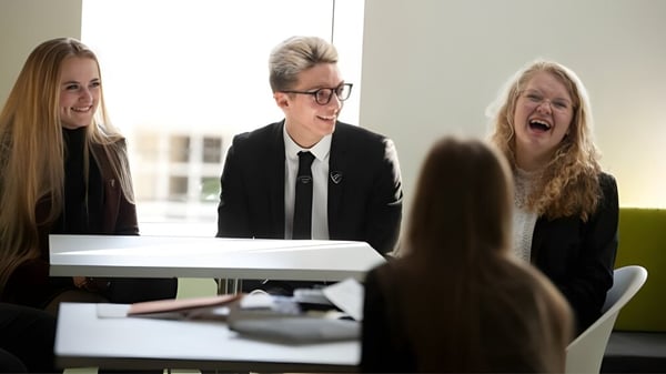 Tres estudiantes de la Fulneck School están sentados en ropa formal en una mesa en una sala de reuniones moderna.