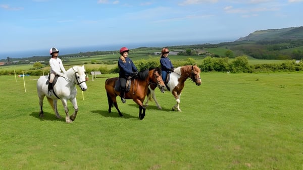 Tres personas montan a caballo en un campo con paisaje rural de fondo en el terreno de la Fyling Hall School.