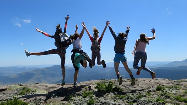 Un grupo de estudiantes del Galway Community College salta en un saliente rocoso frente a un paisaje montañoso.