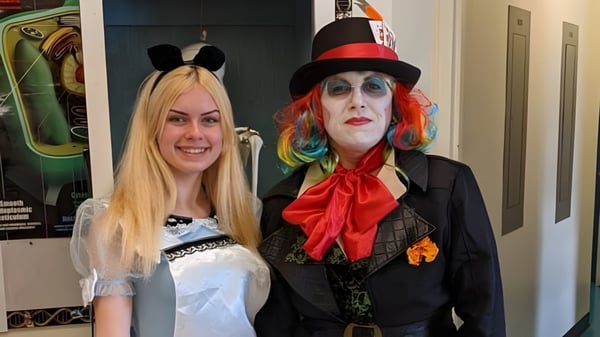Dos personas en coloridos disfraces de teatro están de pie en una sala en el campus de Gander Collegiate.