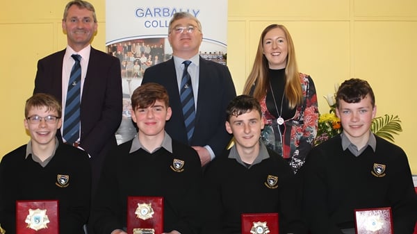 Un grupo de alumnas y alumnos con dos responsables escolares posan frente a una pancarta del Garbally College.