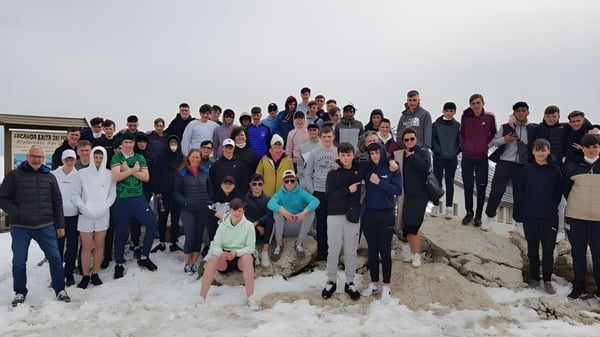 Un gran grupo de personas está reunido en el Garbally College en un paisaje nevado bajo un cielo nublado.