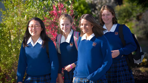 Cuatro alumnas en uniformes escolares están juntas en un jardín en el campus del Garin College.