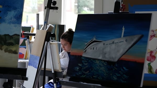 Un estudiante pinta en un caballete en la clase de arte de la Garrison Forest School con materiales de arte en la sala.