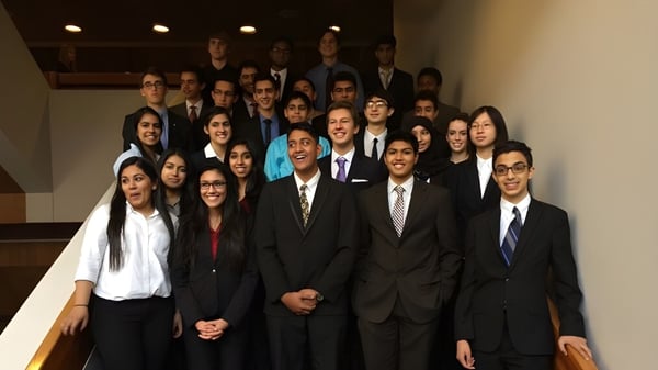 Un grupo de estudiantes de la Garth Webb Secondary School está vestido de manera formal frente a una escalera de madera.