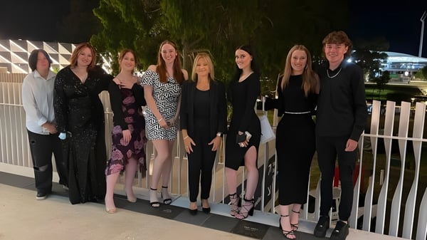 Un grupo de estudiantes bien vestidos está de pie por la noche con árboles de fondo en el terreno del Gawler and District College.