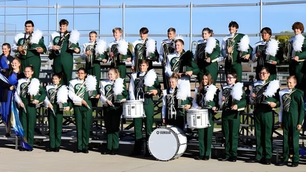 Estudiantes de la Gehlen Catholic School posan con sus instrumentos frente a un edificio de vidrio.