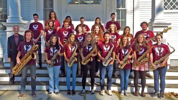 Estudiantes de la George Stevens Academy están en uniformes rojos con instrumentos musicales en las escaleras de un edificio con columnas.