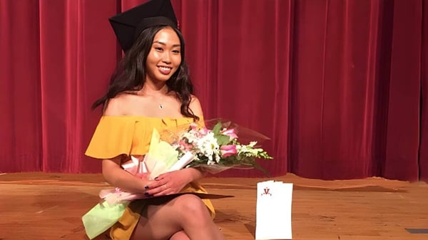 Una graduada de la Georges Vanier Secondary School está frente a una cortina roja y sostiene un ramo de flores en la mano.
