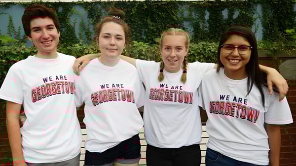Cuatro estudiantes de Georgetown District High School están juntos frente a un fondo de seto verde y llevan camisetas blancas con la impresión We are Georgetown.