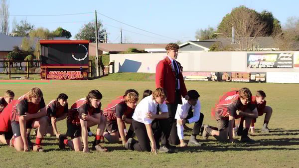 Un grupo de estudiantes de la Geraldine High School se reúne en el campo deportivo frente a un remolque rojo y edificios.