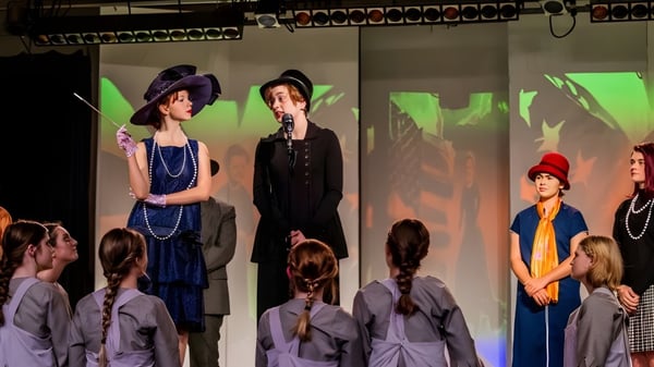 Alumnas de la Girls Preparatory School presentan una obra de teatro con trajes históricos en un escenario con iluminación colorida.