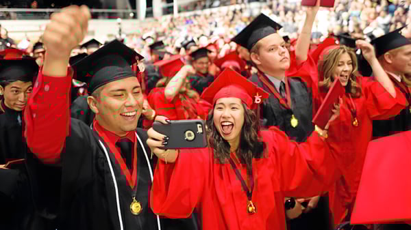 Un gran grupo de graduadas y graduados de la Gladstone Secondary School celebra su graduación en togas rojas y toma selfies.