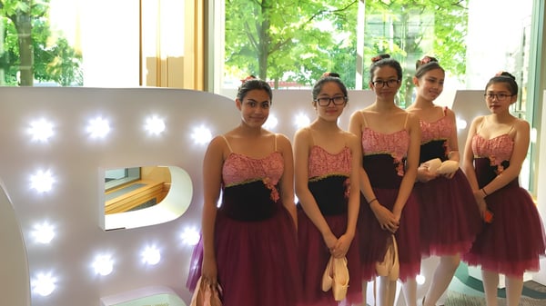 Un grupo de jóvenes mujeres en vestidos elegantes se encuentra frente a una gran letra P iluminada en el campus de la Gladstone Secondary School.