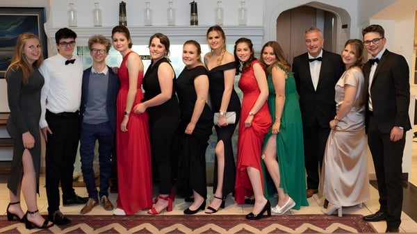 Un grupo de estudiantes elegantemente vestidos está en el Glenalmond College frente a un fondo decorativo.