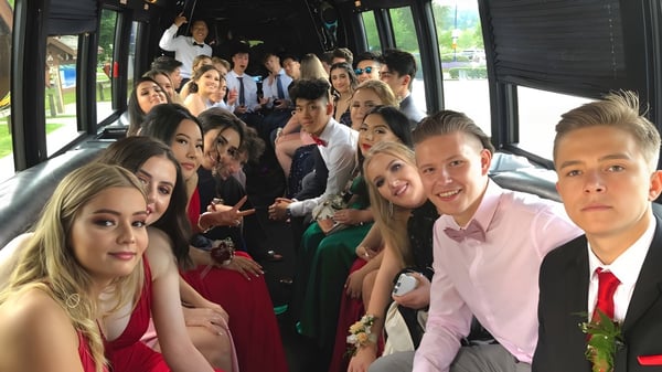Un grupo de estudiantes de la Gleneagle Secondary School en ropa formal está sentado juntos en un autobús al aire libre.
