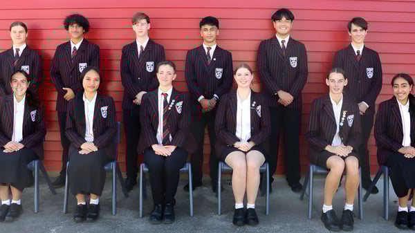 Un grupo de estudiantes del Glenfield College está frente a una pared de madera roja.