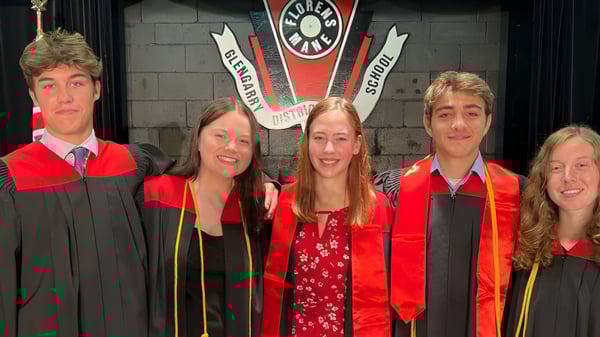 Cinco estudiantes de Glengarry District High School están en ropa de graduación frente a un escudo universitario.