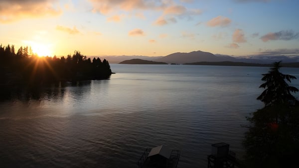 Un lago tranquilo con bosques perennes y montañas al fondo durante el atardecer en el campus de la Glenlyon Norfolk School.