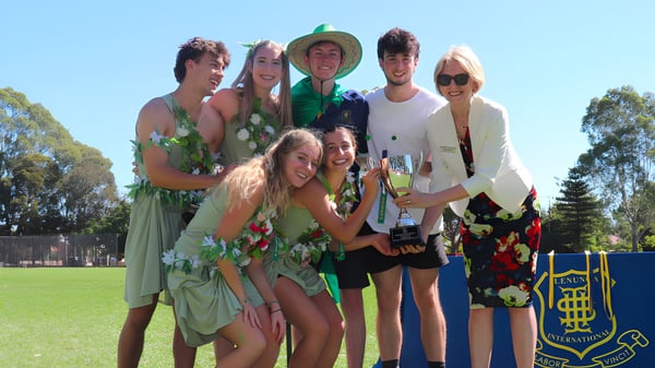 Un grupo de estudiantes de la Glenunga International High School está en una pradera frente a unos árboles.