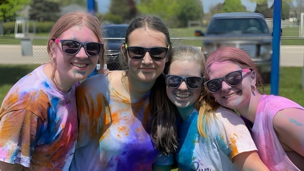 Un grupo de jóvenes mujeres con camisetas de batik coloridas posan juntas al aire libre en el terreno del Goderich District Collegiate Institute.