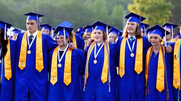 Un grupo de graduados con túnicas azules y doradas está reunido frente a un paisaje natural en el campus del Goderich District Collegiate Institute.