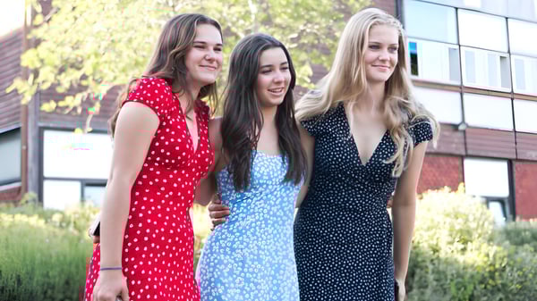 Tres alumnas de la Godolphin School están juntas frente a un edificio con plantas verdes de fondo.