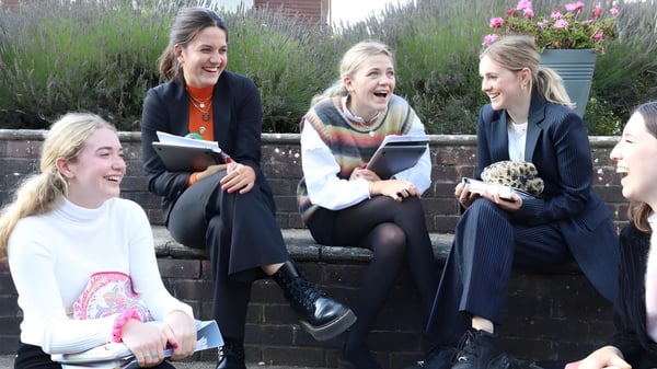 Cuatro alumnas de la Godolphin School están sentadas en un muro y conversando en un entorno verde.