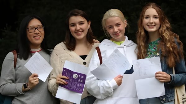 Cuatro alumnas de la Godolphin School sostienen papeles sonriendo frente a un fondo oscuro.
